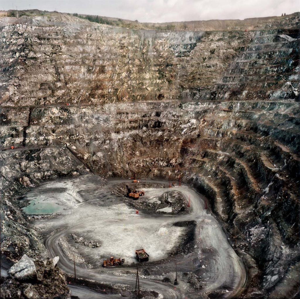 Looking downward into mine pit with high grey sides of scraped rock